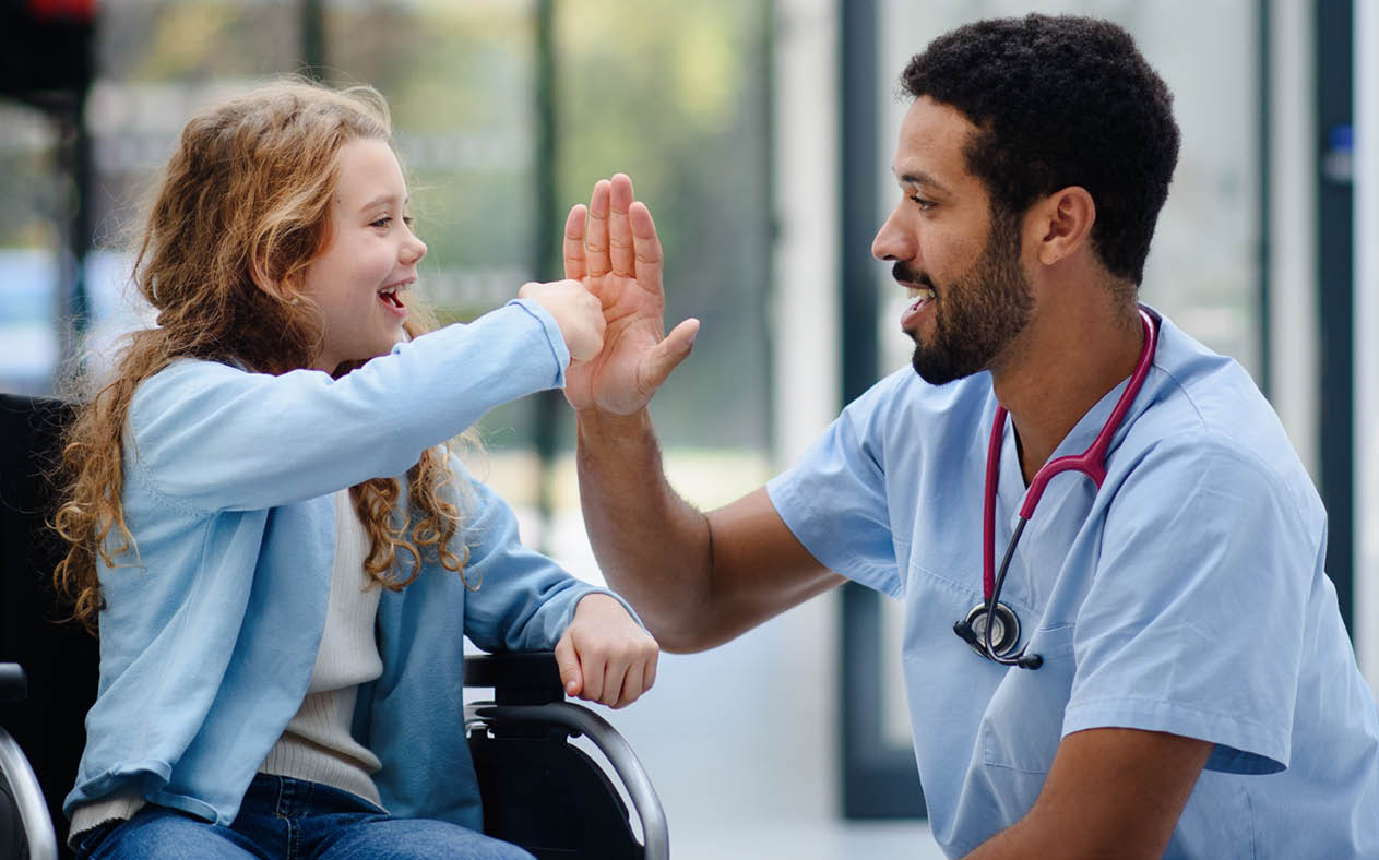 Young multiracial doctor having fun with little girl on a wheelchair.