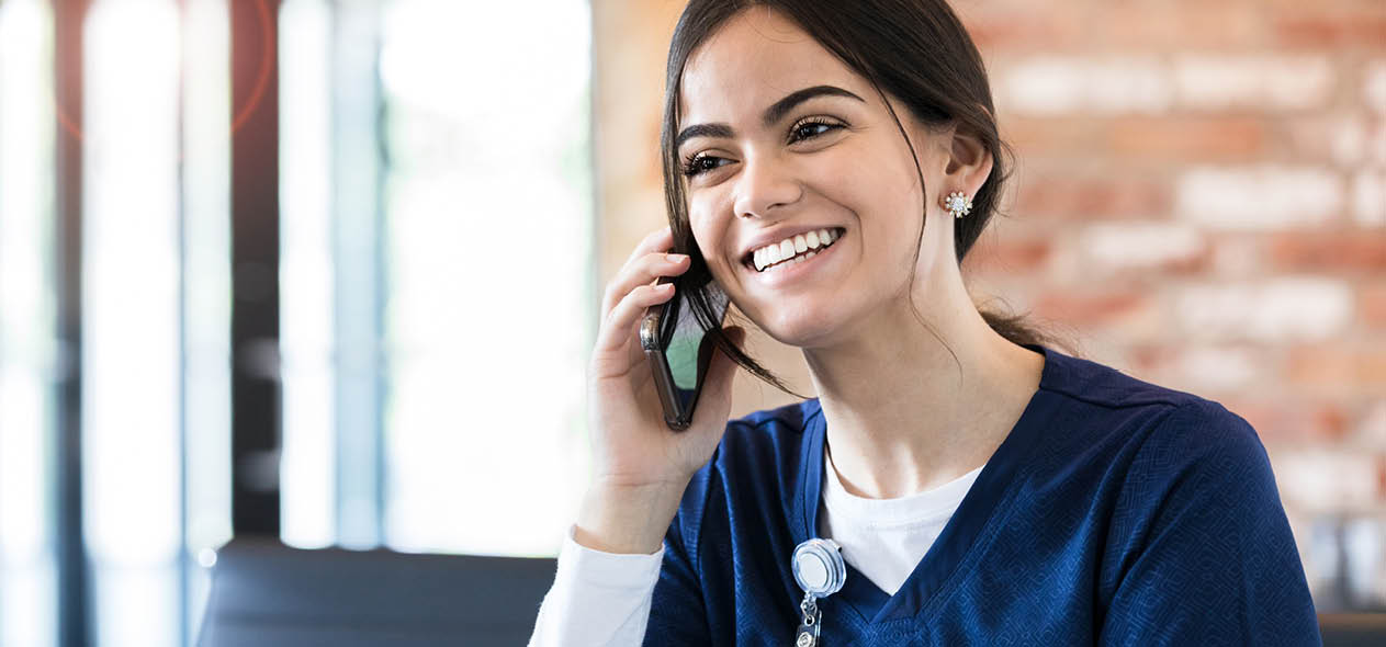 Taking a break with a cup of coffee, the young female nurse talks on her smart phone.